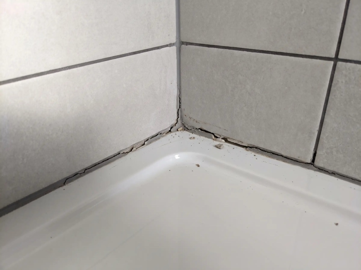 Cracked grout where the shower tray meets the tiles, circled in red with the note “regrout all of it”